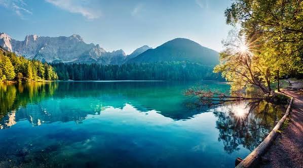 Lac de montagne turquoise entouré de forêts et de sommets au lever du soleil